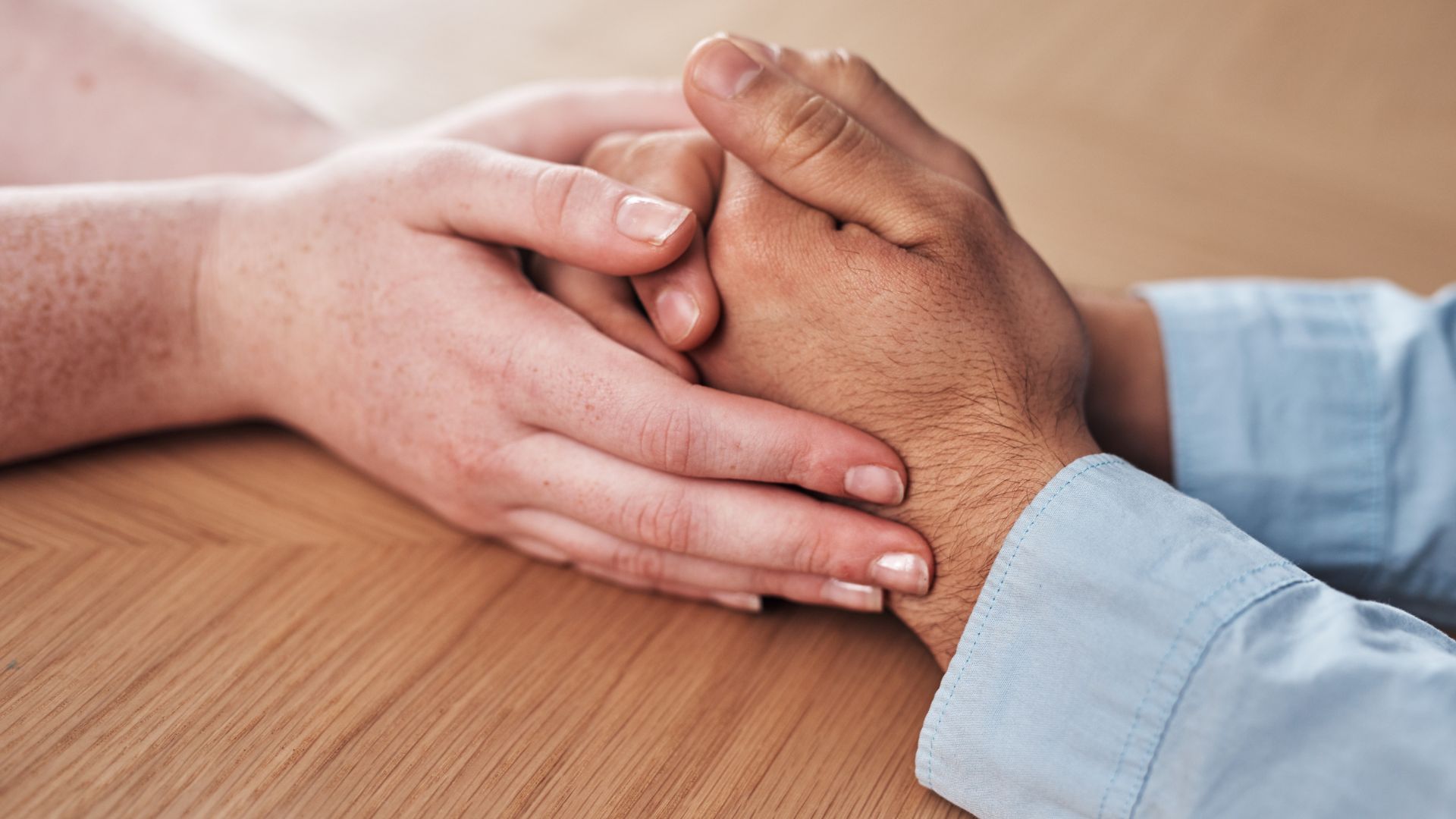 Close-up of two hands clasped together in a supportive, comforting gesture on a wooden surface